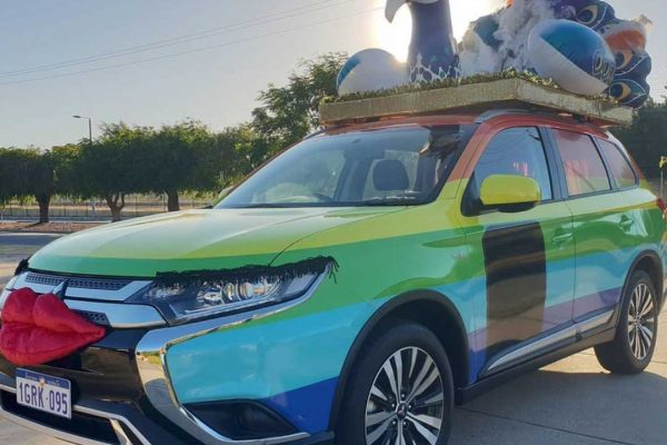 SUV vehicle parked in driveway decorated with a rainbow themed vinyl wrap and a peacock on the roof