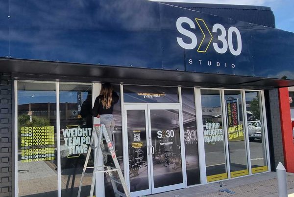 Gym shop front with blue sign printing for SX30 with a man on a ladder installing stickers